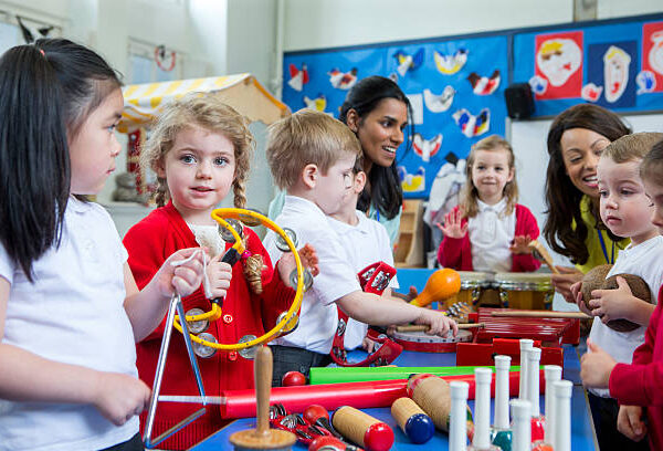 Nursery children playing with musical instruments in the classroom. One little girl is looking at the camera with a tambourine.